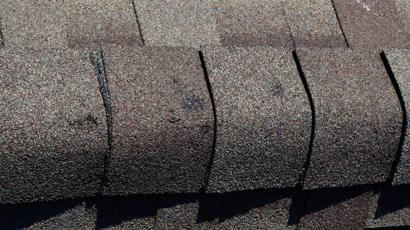 Brown toned ridge cap shingles on a sunlit asphalt roof