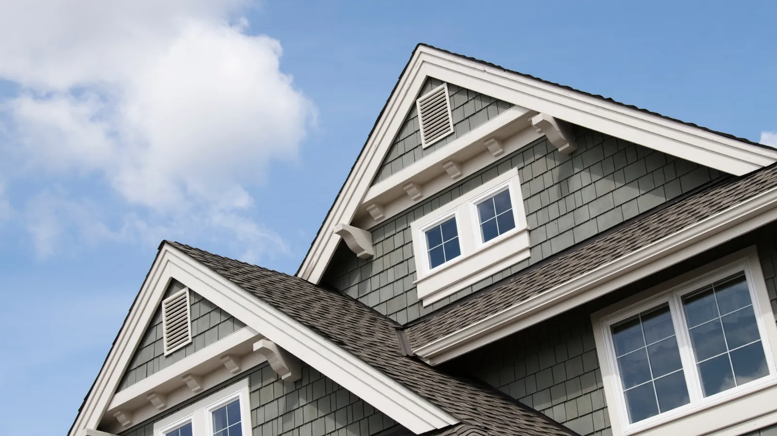 Brown shingle roof below house gables with white trim