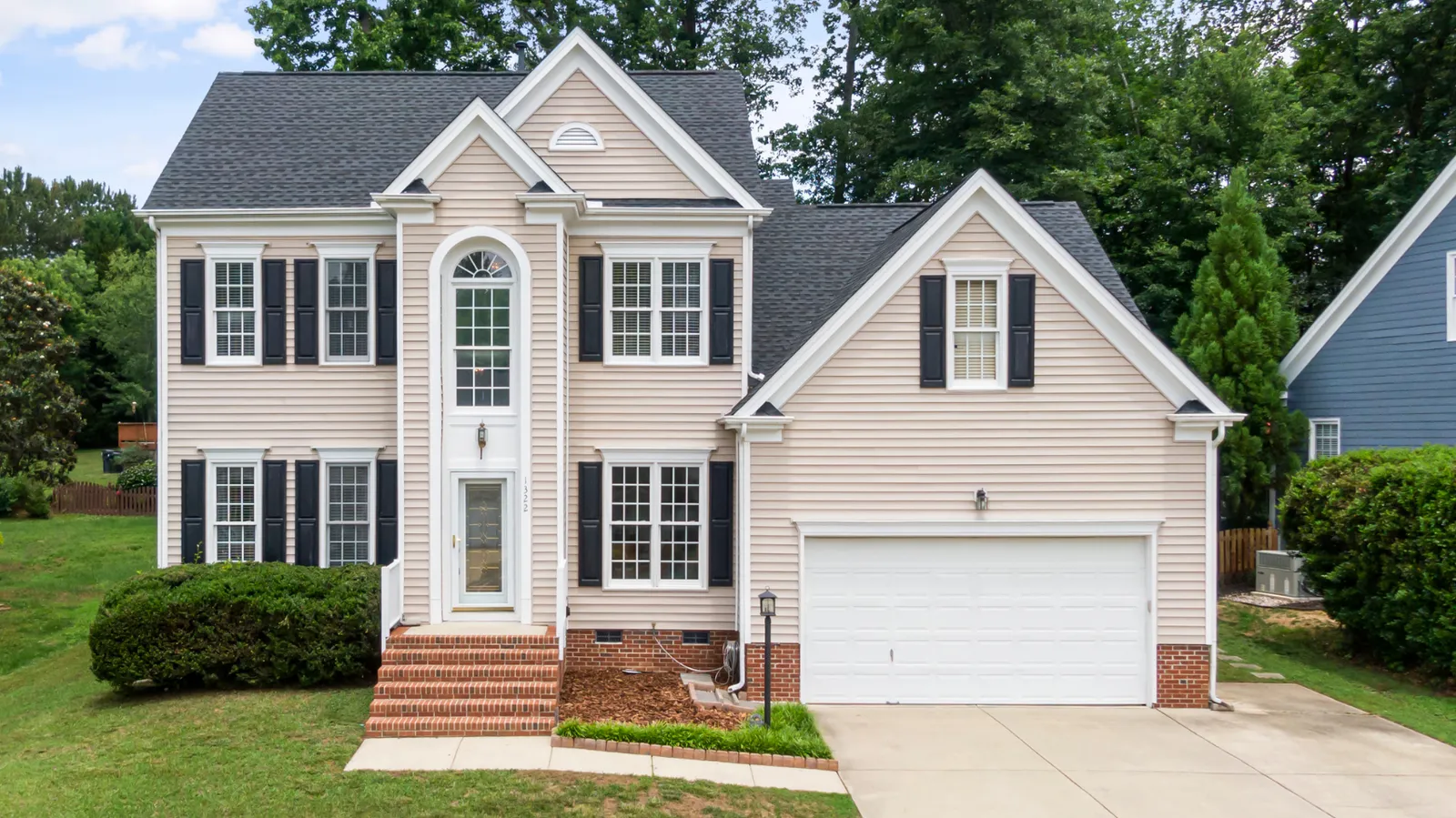 Black shuttered beige two-story home beneath a dark shingle roof