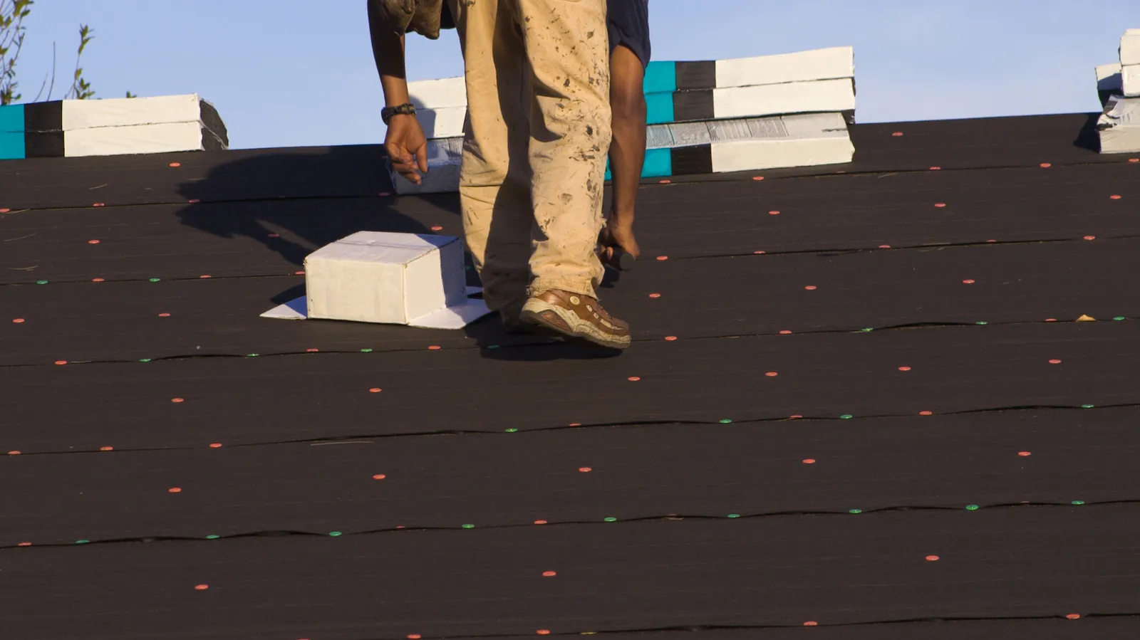 Stacked shingle bundles near a roofer walking across underlayment