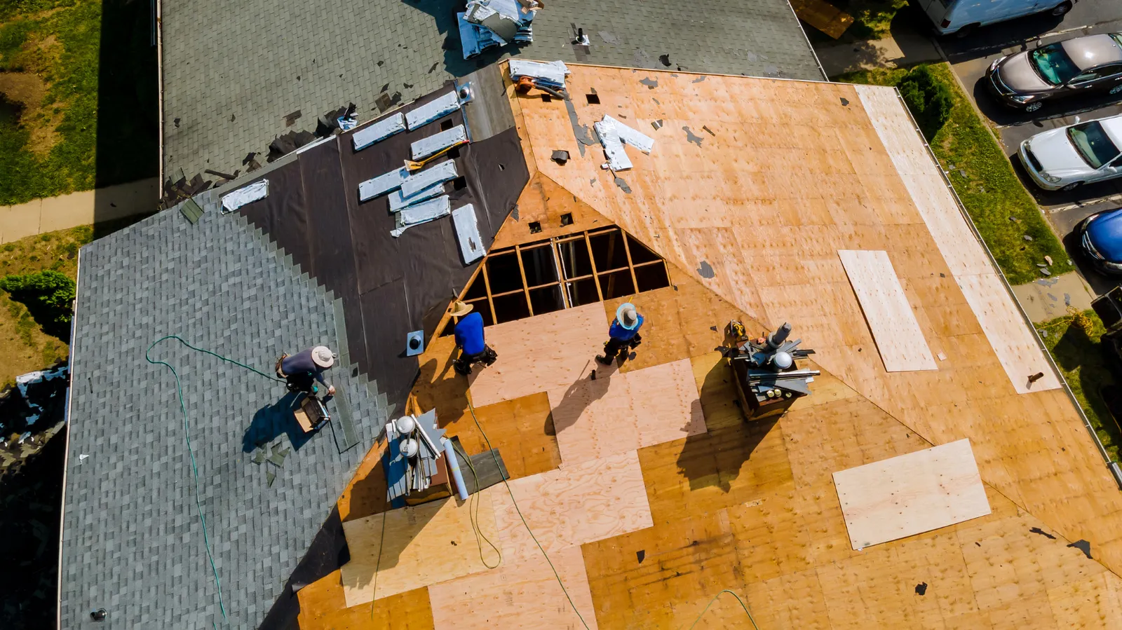 Roofers replacing shingles on a large roof seen from overhead