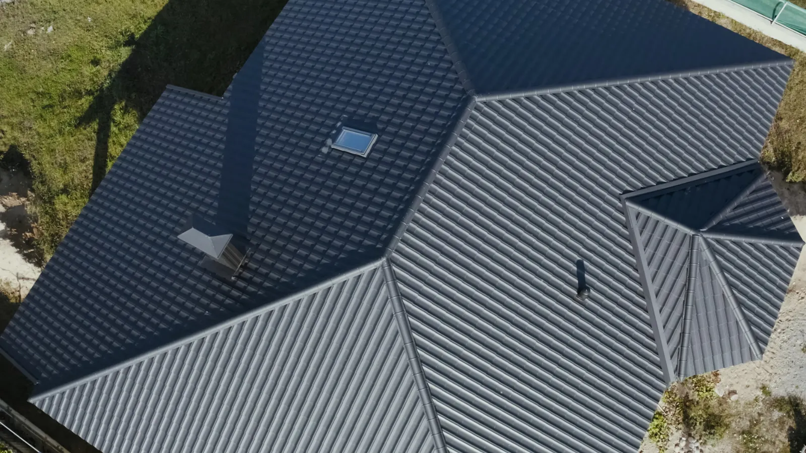 Charcoal metal tile roof slopes meeting above a brick gable and gutter